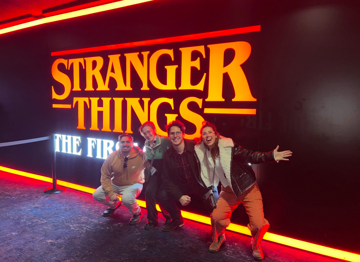 four people in front of a Stranger Things: The First Shadow sign